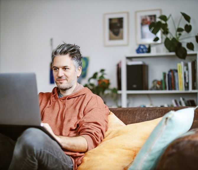 Mies istuu rennosti sohvalla tietokone sylissään