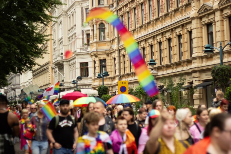 Helsinki Pride -kulkue kulkemassa kantakaupungissa. Taustalla näkyy rakennuksia ja etualalla kulkueen osallistujia.