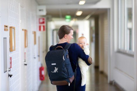 Nainen reppu selässään pitää sylissään pientä lasta, joka vilkuttaa kuvaajalle