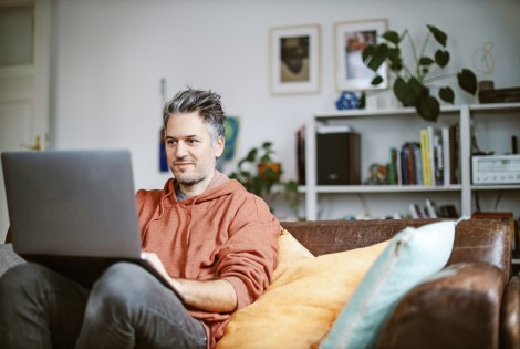 Mies istuu rennosti sohvalla tietokone sylissään