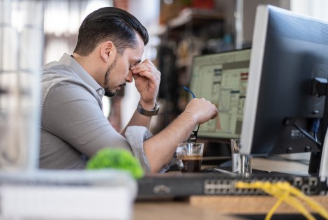 Mies istuu tietokoneen ääressä väsyneen näköisenä.